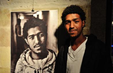 Un migrant pose devant son portrait
